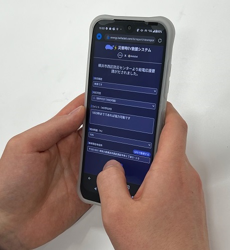 男性の手が持つスマートフォンに映った災害時EV救援アプリの画面（画面は開発中です）